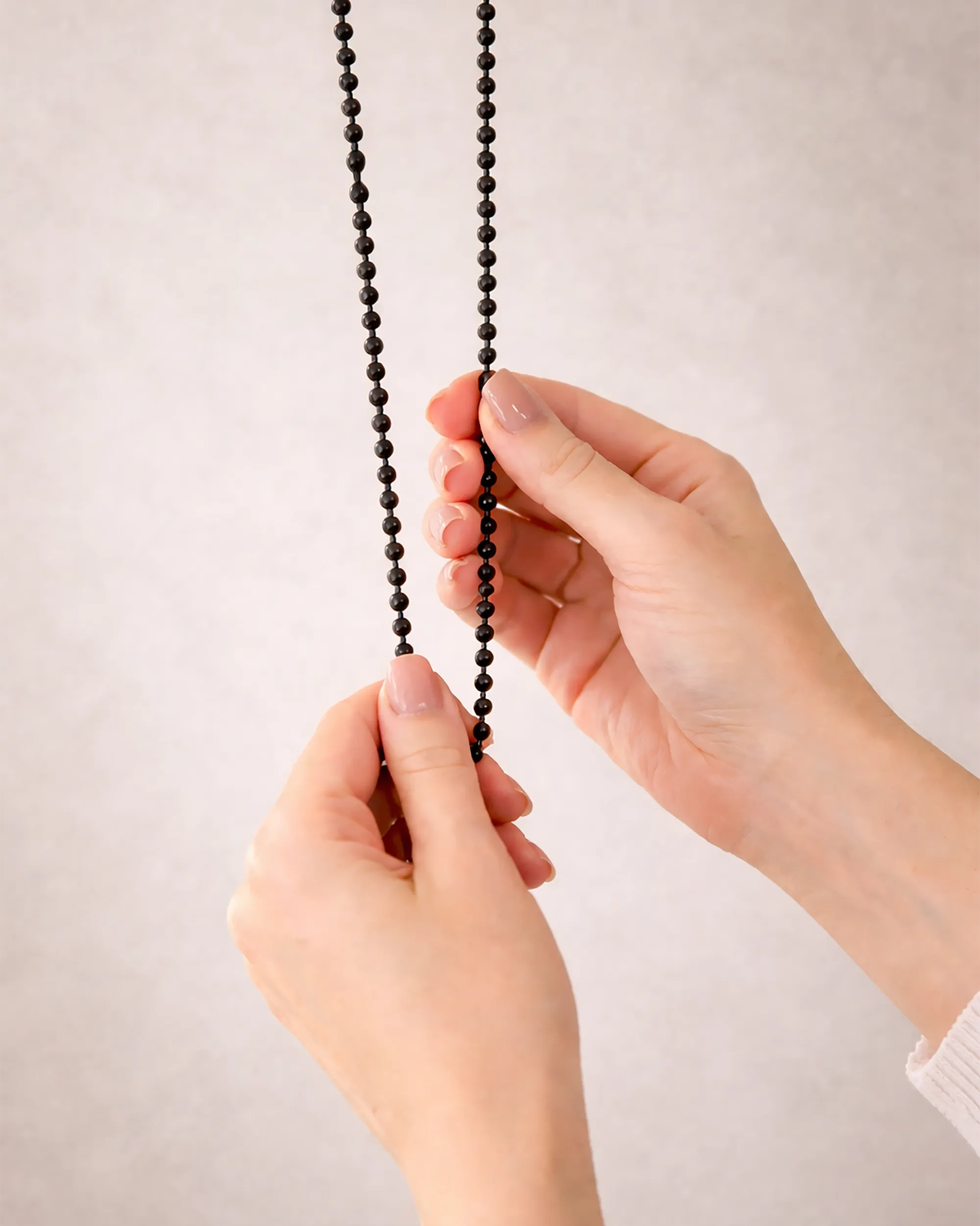 Corrente de acionamento manual preta para persiana sob medida, em close, sendo manuseada por mãos, com acabamento escuro