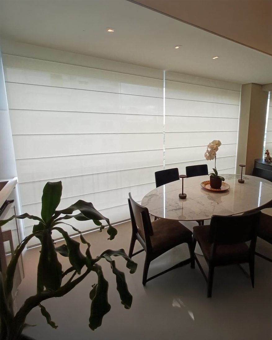 Cortina romana em tela solar 3% branca instalada em ampla sala de jantar, proporcionando controle da luminosidade, conforto visual e estética limpa. O tecido permite a entrada de luz natural de forma equilibrada, mantendo privacidade e integração com o ambiente.