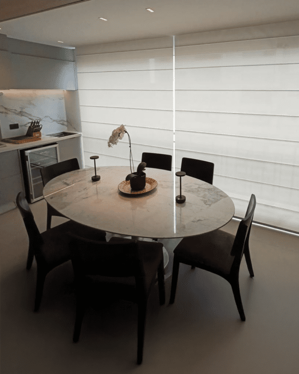 Cortina romana em tela solar 3% branca instalada em sala de jantar com mesa redonda e iluminação natural suave.