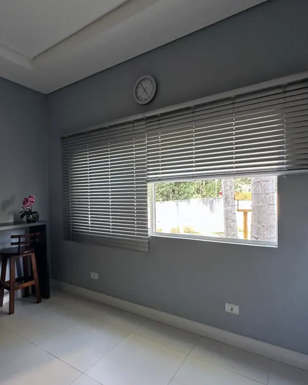 Persiana horizontal de alumínio 50mm na cor prata fosca instalada em ambiente interno, com lâminas parcialmente fechadas e controle de luz natural.