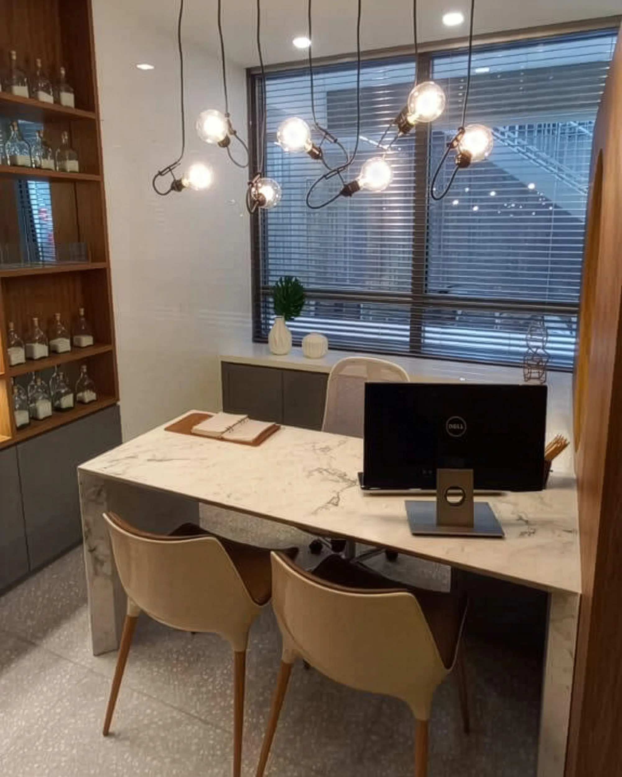 Persiana horizontal de alumínio 50mm prata fosca com lâminas inclinadas em ambiente de clínica, filtrando a luz natural