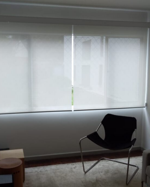 Persiana Rolô Tela Solar 3% Branca instalada em sala de estar com controle da luminosidade e vista para o exterior