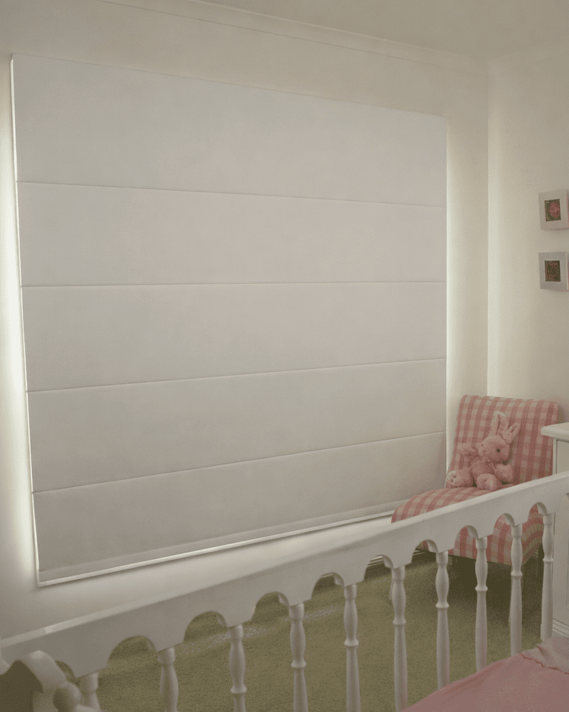 Persiana Romana Blackout Nápoles branca totalmente fechada em quarto de bebê, proporcionando bloqueio de luz e conforto no ambiente.